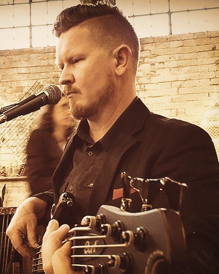 Lukas playing at the microphone in a brick-walled venue